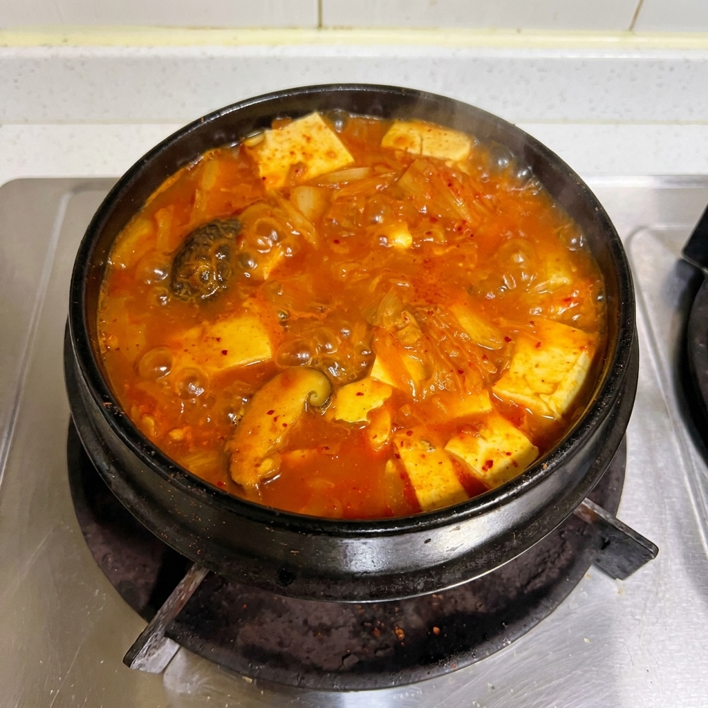 Ein farbenfroher roter Kimchi-Thunfisch-Eintopf kocht kräftig in einem traditionellen Steintopf auf dem Herd.