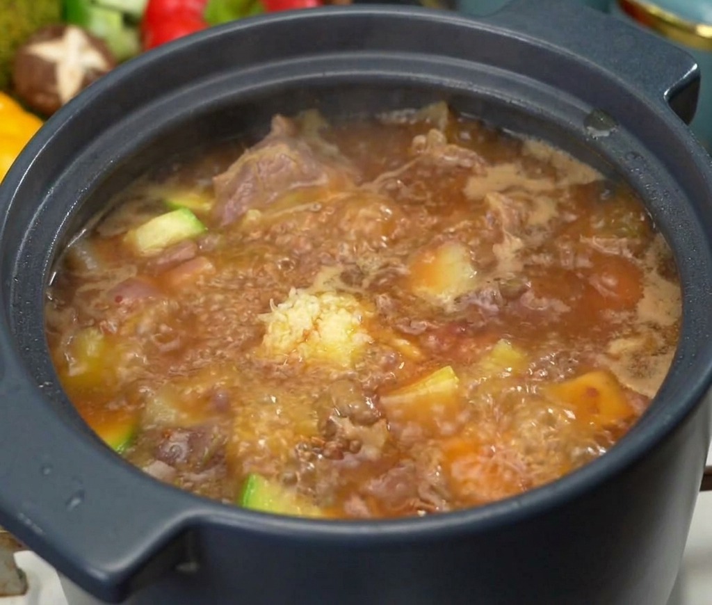Ein Löffel gehackter Knoblauch wird in den kochenden Eintopf mit Rindfleisch und Zucchini gegeben.