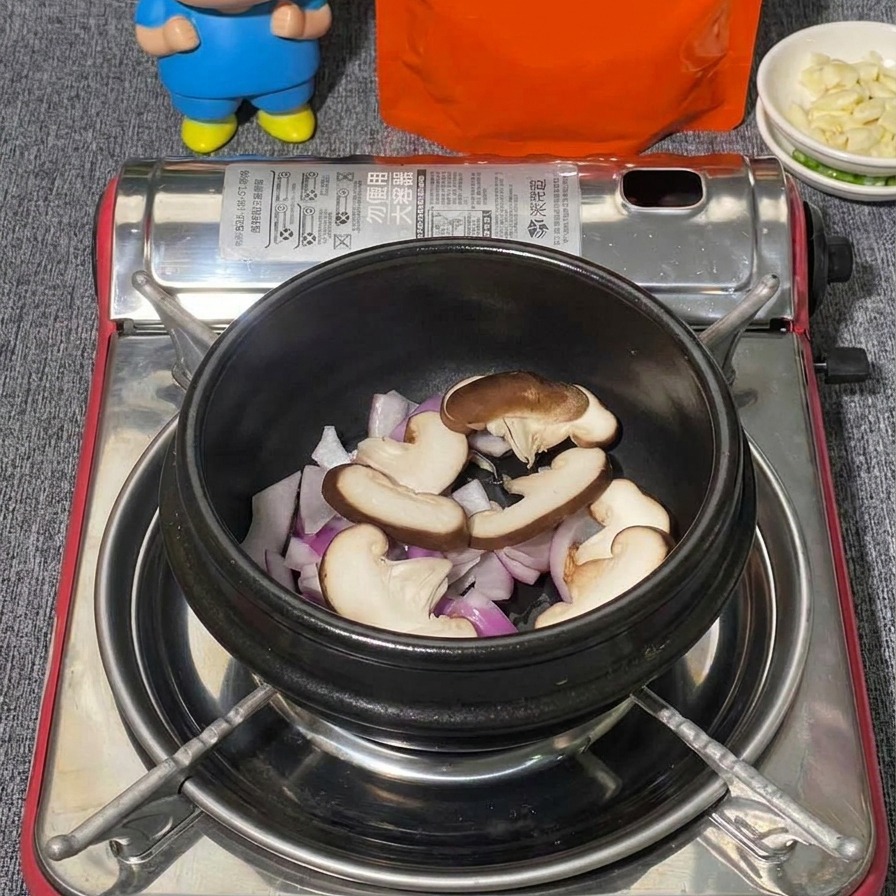 Verschiedene Pilze, darunter geschnittene Shiitake und weiße Shimeji-Pilze, werden über roten Zwiebeln in einem schwarzen Steintopf geschichtet.