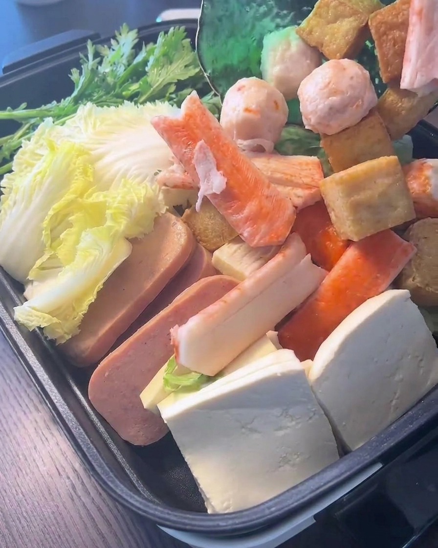 Verschiedene Fischbällchen und Surimi-Sticks werden auf frischem Blattgemüse und Chinakohl im Kochtopf platziert.
