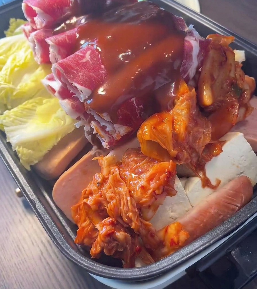 Reichhaltige, rote koreanische Chilisauce wird über einen mit Rindfleisch, Kimchi und Gemüse geschichteten Topf gegossen.