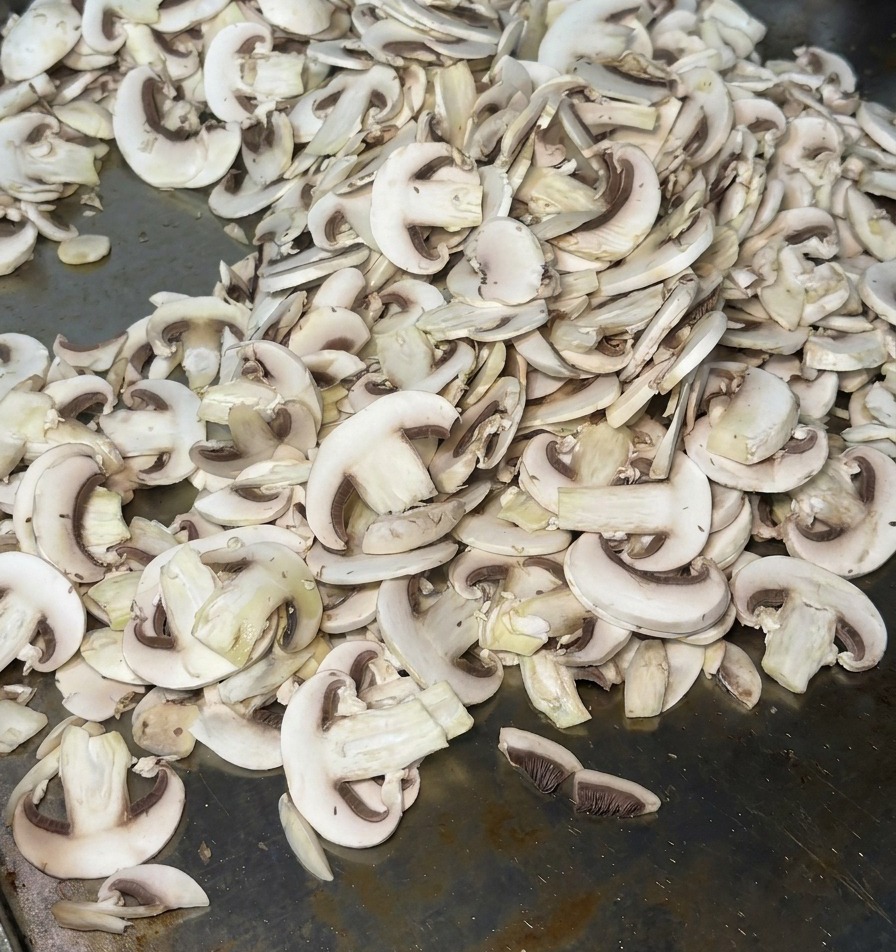 Dünn geschnittene Champignons auf einer heißen Grillplatte, die beim Garen Dampf abgeben.