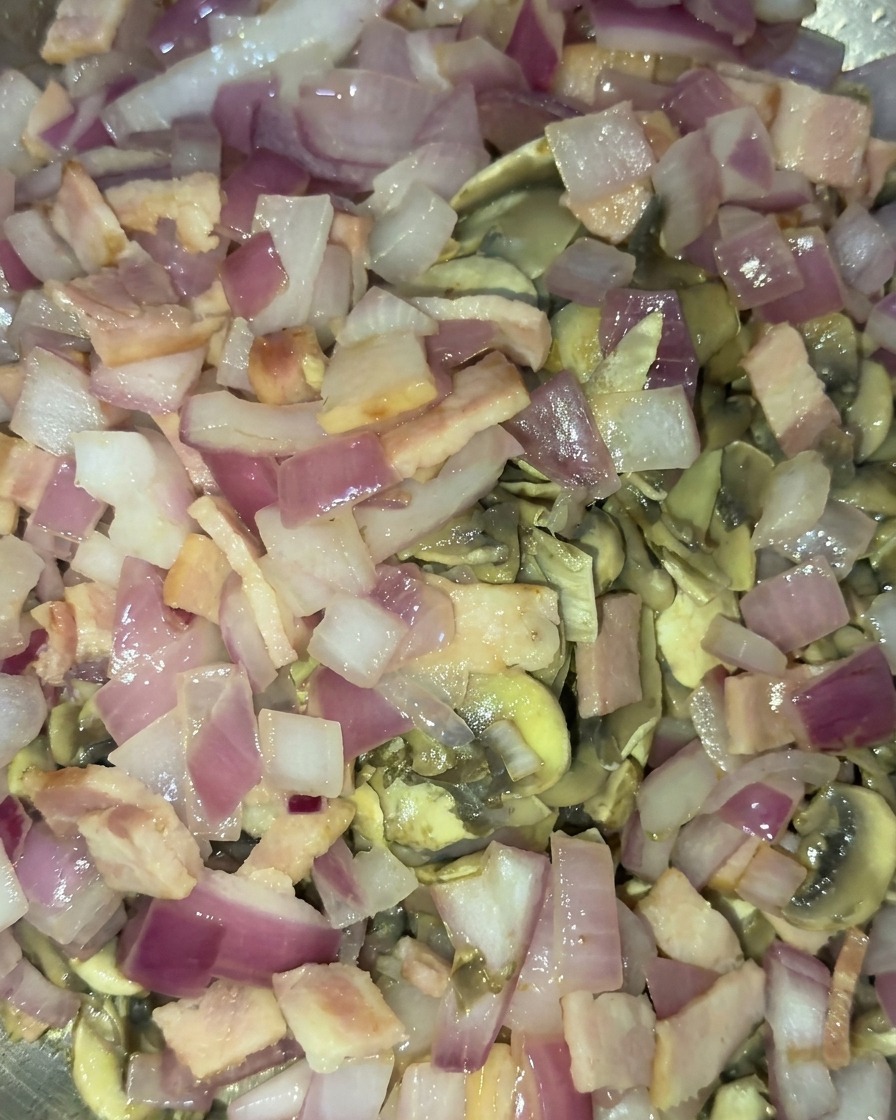 Eine kombinierte Mischung aus goldbraun angebratenen Champignons, glasigen roten Zwiebeln und Speckwürfeln wird zusammen angebraten.