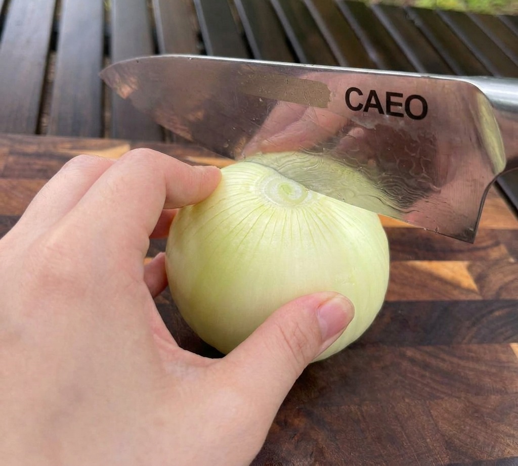 Eine Hand hält eine weiße Zwiebel auf einem Holzschneidebrett, während ein Kochmesser sie in Scheiben schneidet.