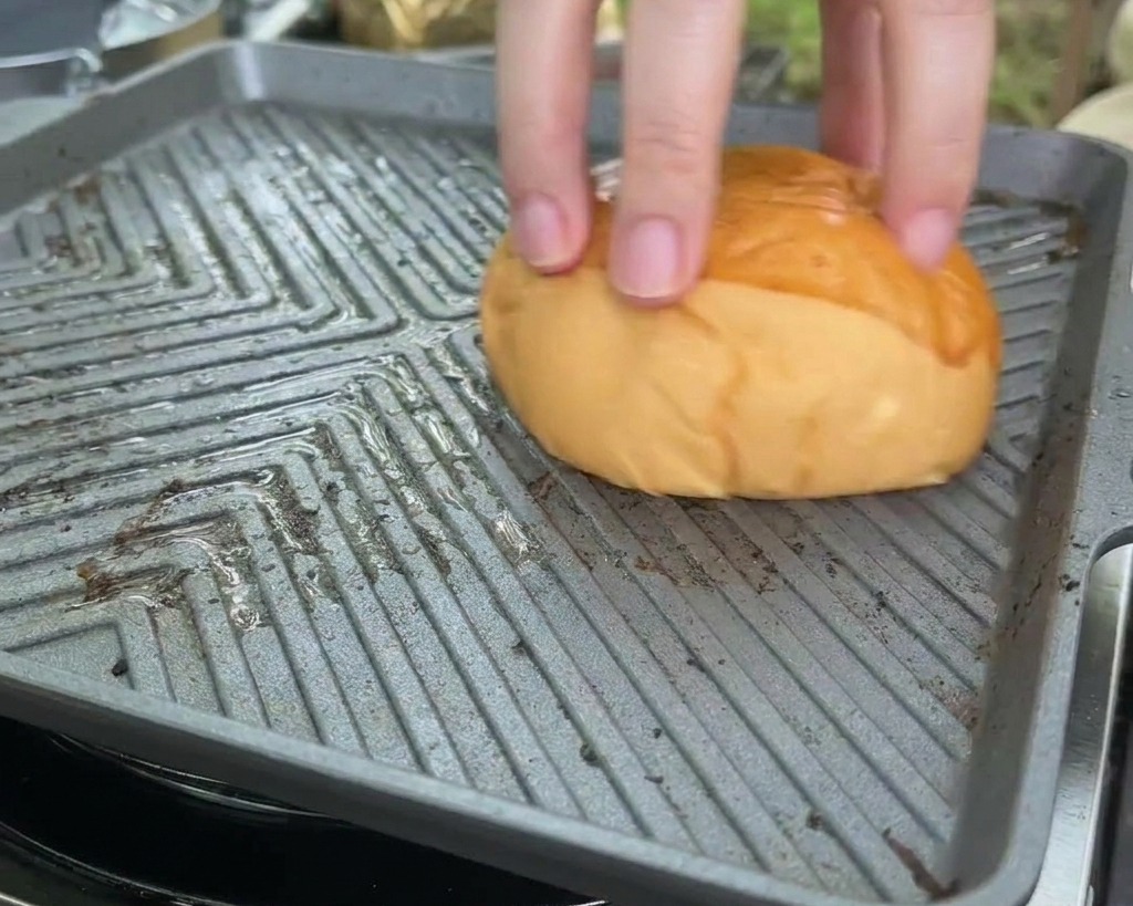 Ein Brioche-Brötchen wird mit der Schnittfläche nach unten auf eine heiße, viereckige Grillpfanne gedrückt.