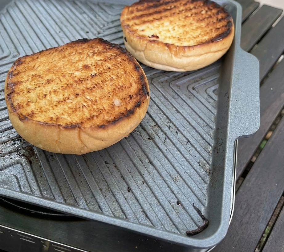 Ein silberner Löffel verstreicht dicke cremige rosa Sauce auf der goldbraunen Schnittfläche eines getoasteten Brioche-Brötchens.
