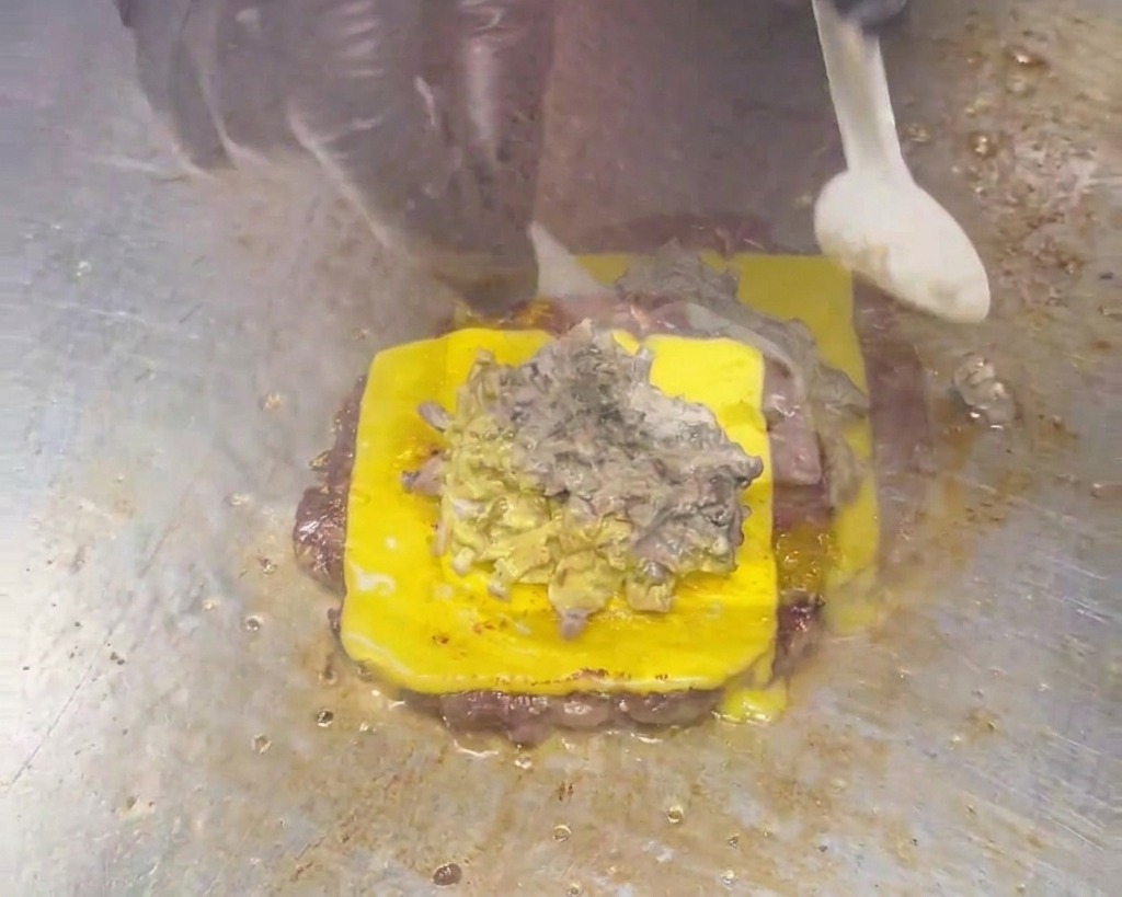 Ein Löffel verteilt eine dicke, cremige, graubraune Pilzsauce auf einem Cheeseburger-Patty.