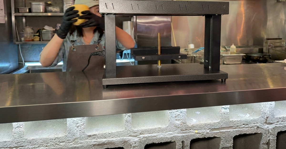 Hände spannen einen halben runden Käselaib in die Halterung eines speziellen Raclette-Geräts ein.