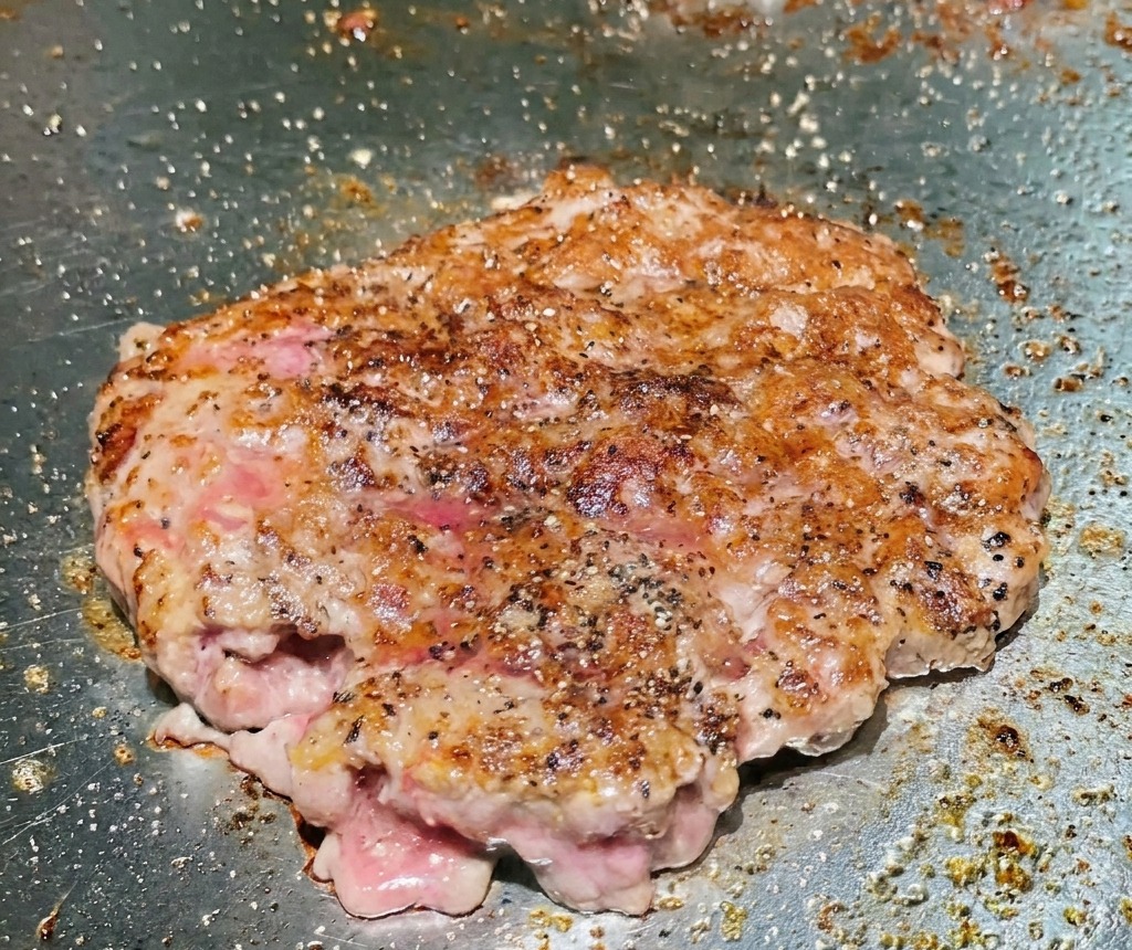 Ein gewendetes Rindfleisch-Patty auf dem Grill zeigt eine kräftig angebratene, braune und knusprige Oberfläche.