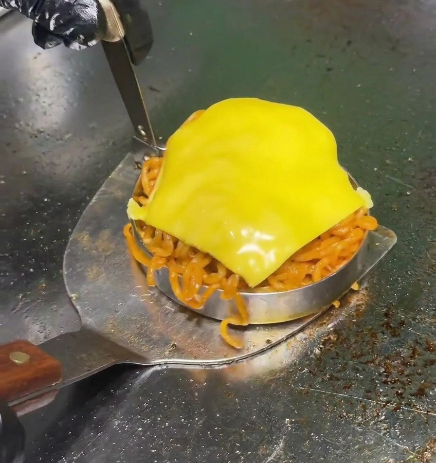 Ein Metallspatel hebt eine runde Form an, die mit scharfen roten Nudeln gefüllt und mit einer Scheibe gelbem Käse getoppt ist.