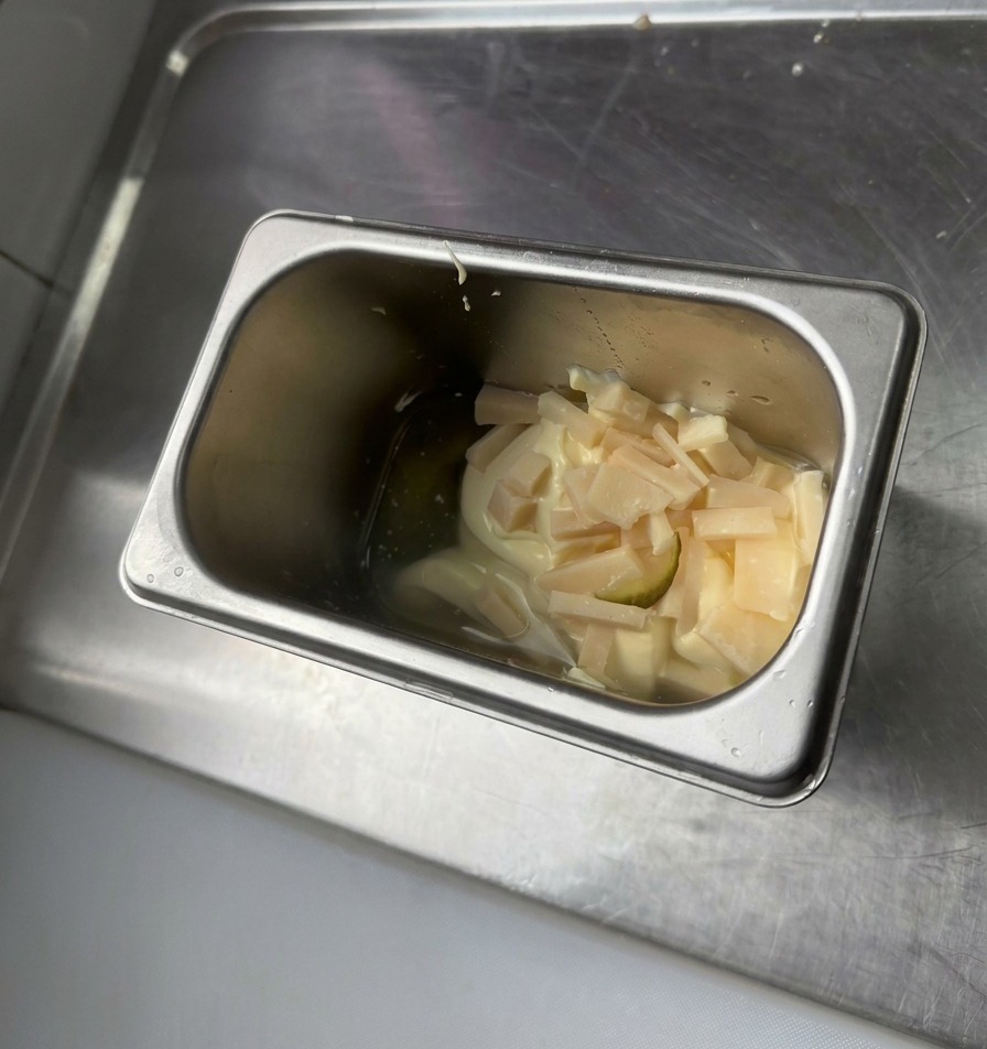 Ein Edelstahlbehälter mit einem Klecks Mayonnaise, gelbem Senf und kleinen, gehackten grünen Gewürzgurken.