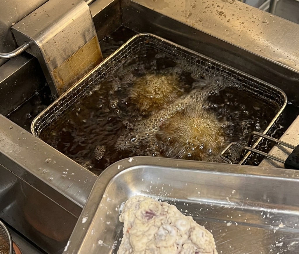 Panierte Hähnchenstücke auf einem Metallblech, bereit, in eine professionelle Fritteuse mit heißem, sprudelndem Öl gegeben zu werden.