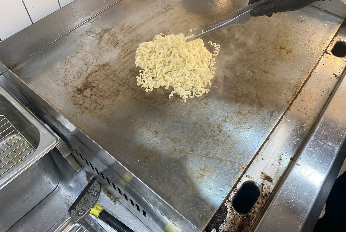 Ein Blick auf dampfende Nudeln und schmelzende Butter auf einer großen, flachen Metallkochfläche.