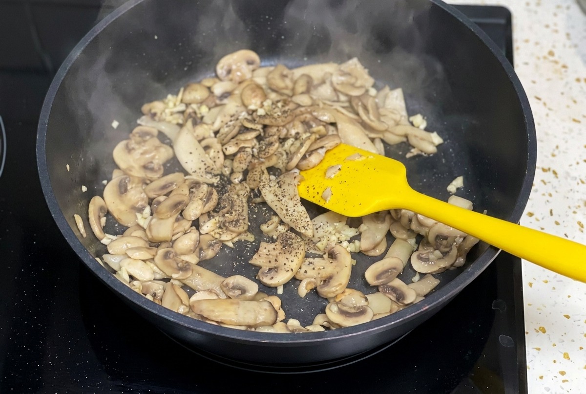 Gebratene Pilze in einer schwarzen Pfanne werden mit gemahlenem schwarzen Pfeffer bestreut.