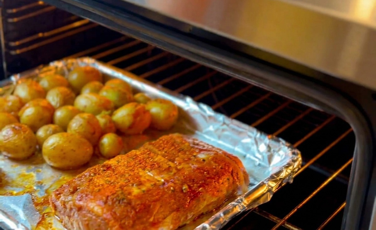Ein Backblech mit Rippchen und kleinen Kartoffeln wird in den Ofen geschoben.