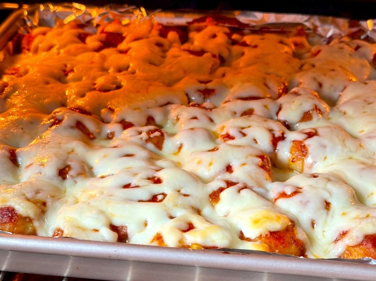 Nahaufnahme von dickem, blubberndem und leicht gebräuntem Käse auf Essen in einem leuchtenden Backofen.