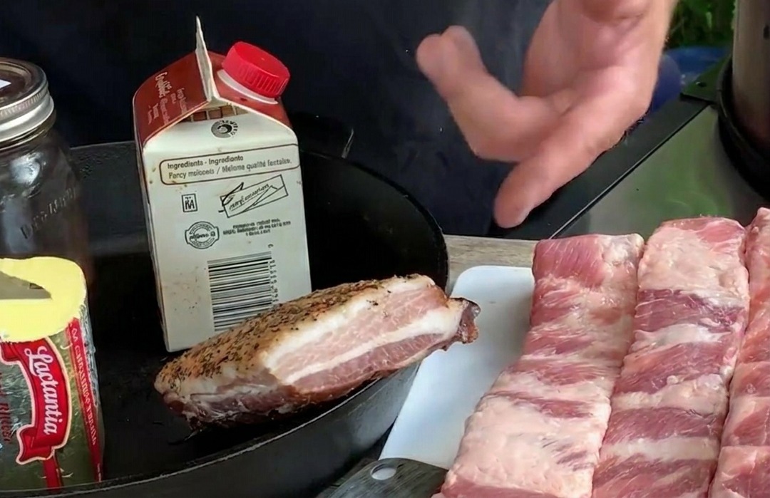 Lange, rohe Schweinerippchen im St. Louis Cut liegen auf einem weißen Schneidebrett neben Butter und frischen Blaubeeren.