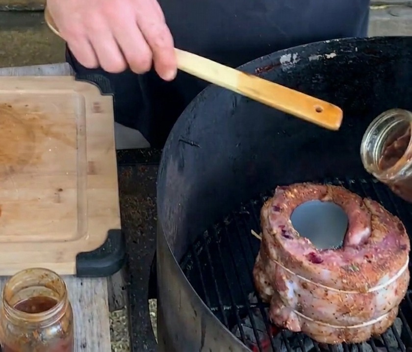 Eine Hand gießt eine dicke, dunkle Blaubeersauce aus einem Glas in eine Metallbierdose, die in einem Rippchen-Becher auf dem Grill steht.