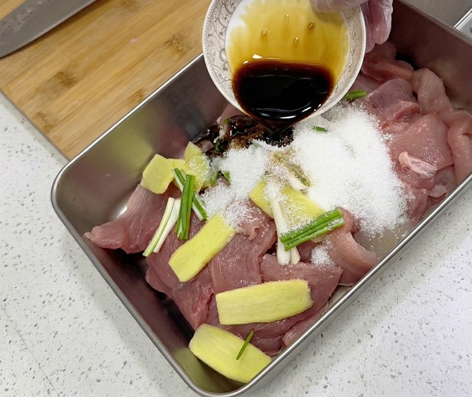 Dunkle flüssige Würzsauce wird aus einer kleinen Schale über rohe Schweinefleischscheiben, Ingwer und Frühlingszwiebeln gegossen.
