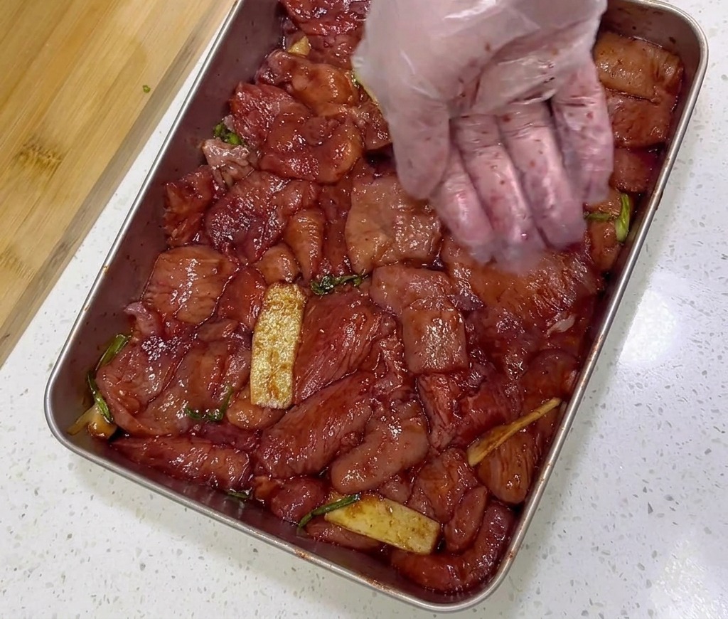 Mariniertes rotes Schweinefleisch wird in einer Edelstahlschale mit einem Löffel grober roter Chiliflocken bestreut.