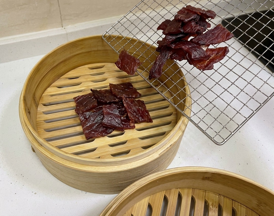 Dunkel rotbraune, luftgetrocknete Schweinefleischstücke werden von einem Kuchengitter in einen runden BAMBUSDÄMPFER gelegt.
