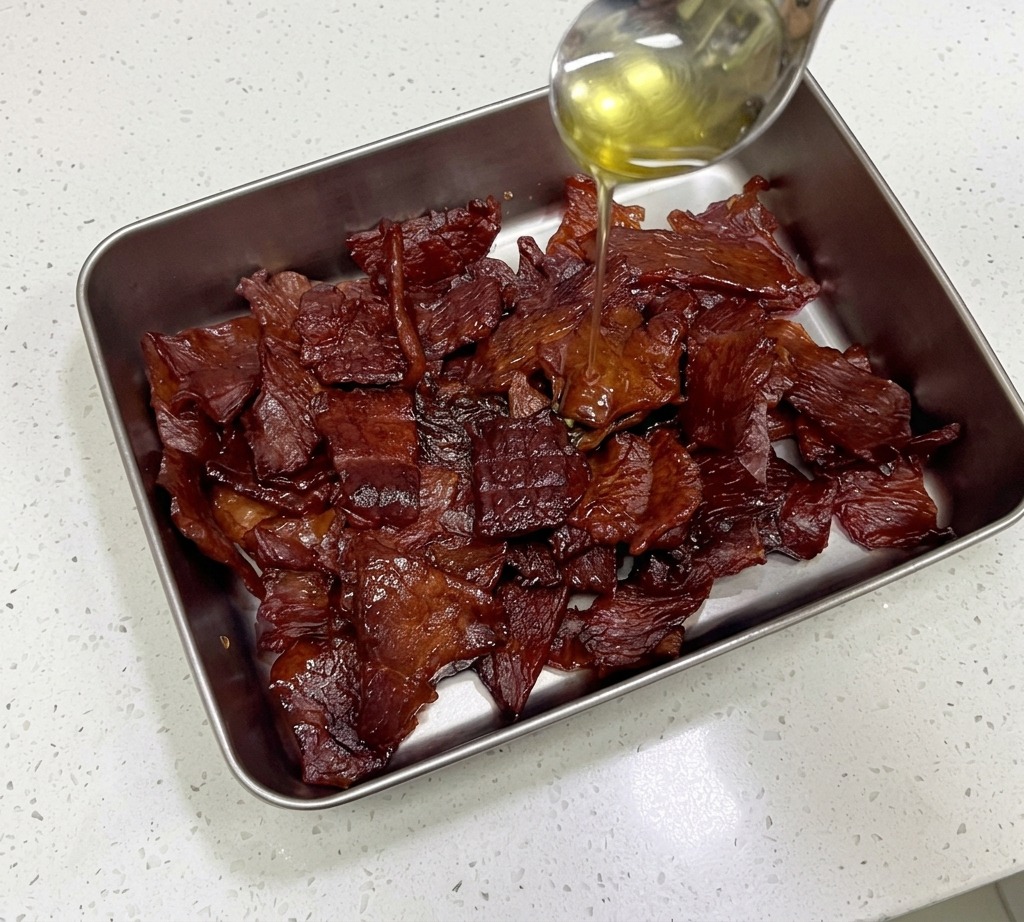 Goldener Honig wird von einem Edelstahllöffel über glänzende, mahagonifarbene Schweine-Jerky-Streifen gegossen.