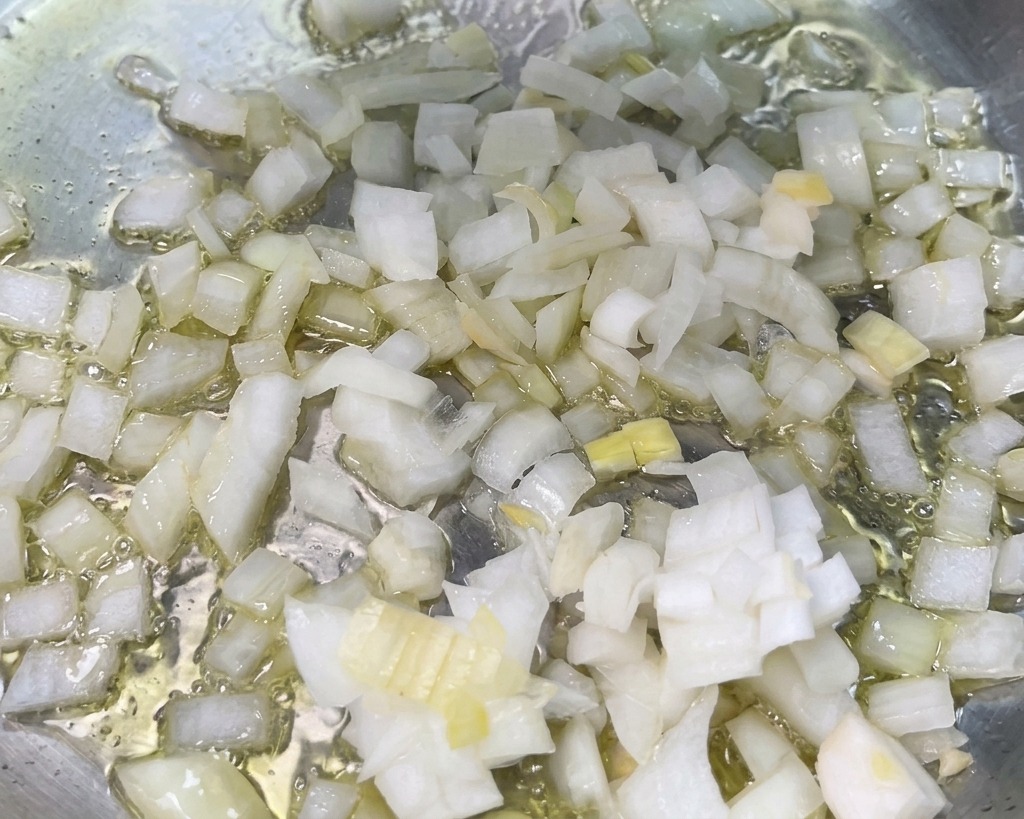 Gewürfelte weiße Zwiebeln braten in heißem Öl auf dem Boden einer Edelstahlpfanne.