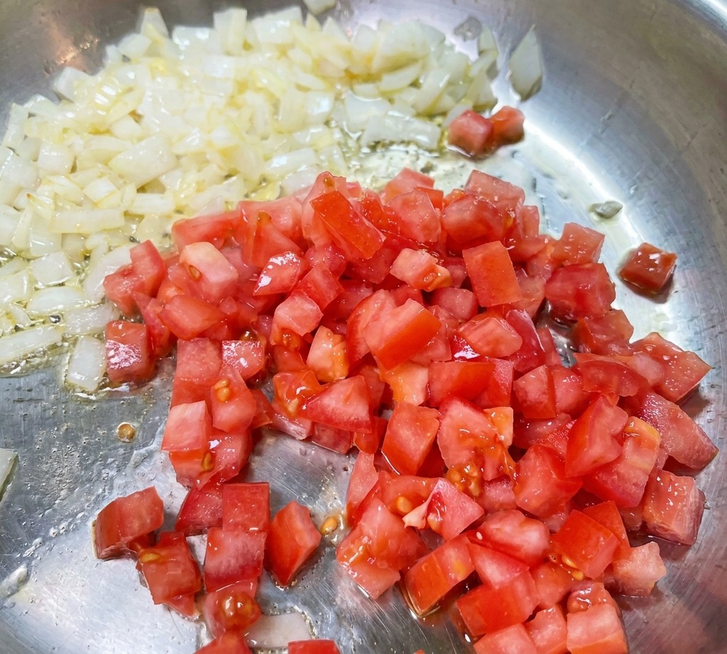 Rote Tomatenwürfel werden in eine Pfanne mit glasig angebratenen Zwiebeln gerührt.