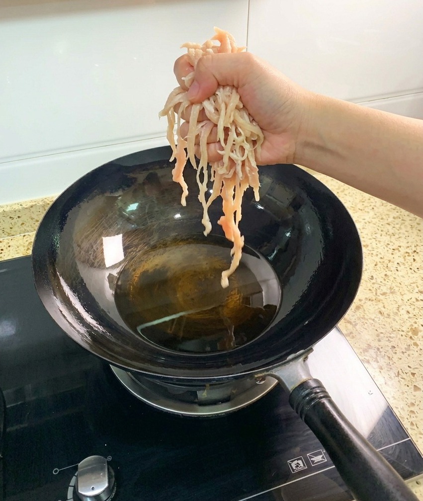 Rohe, in Streifen geschnittene Hähnchenbrust wird in einen heißen Wok mit klarem Bratöl gegeben.