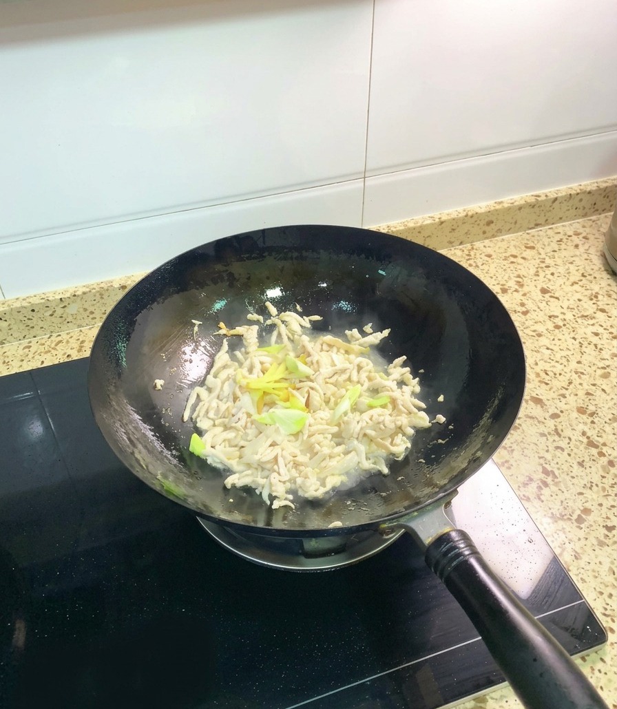 Teilweise gegartes Hähnchenfleisch wird im Wok mit Frühlingszwiebeln und Ingwerstreifen geschwenkt.