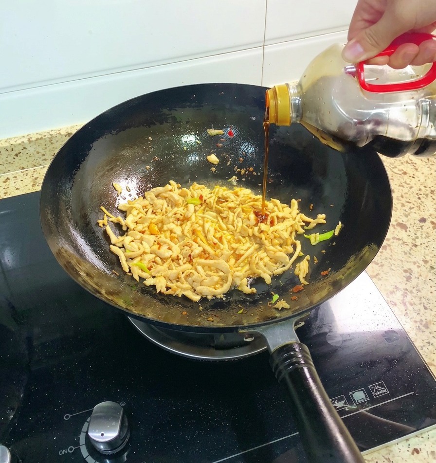 Dunkle Sojasauce wird aus einer Flasche in den Wok zu den Hähnchenstreifen und Frühlingszwiebeln gegossen.
