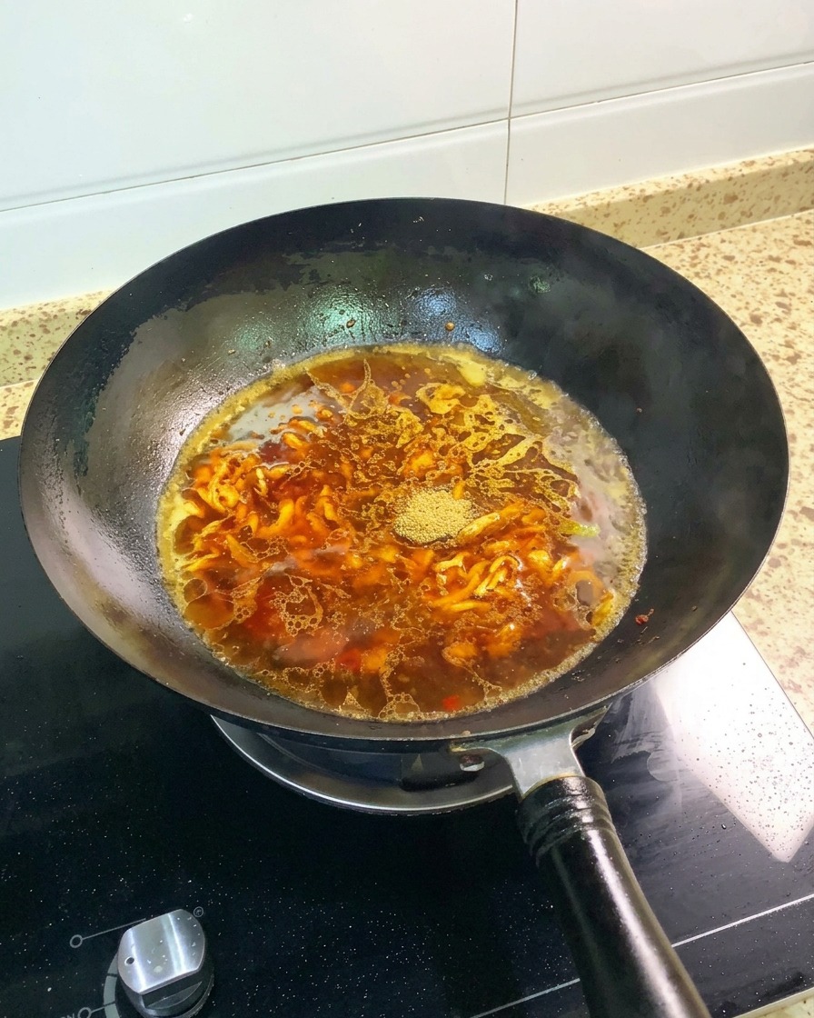 Fünf-Gewürze-Pulver und ein ganzer Sternanis liegen auf der rötlich-braunen Brühe im Wok.