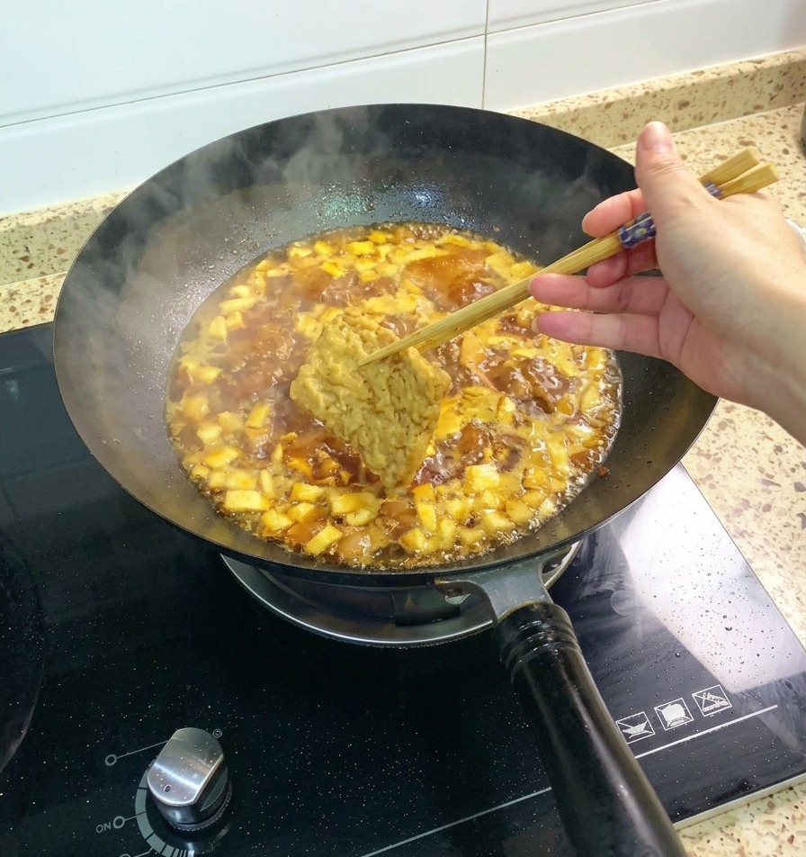 Ein Stück frittierter Tofu wird mit Stäbchen in die blubbernde Hähnchen-Pilz-Sauce getaucht.