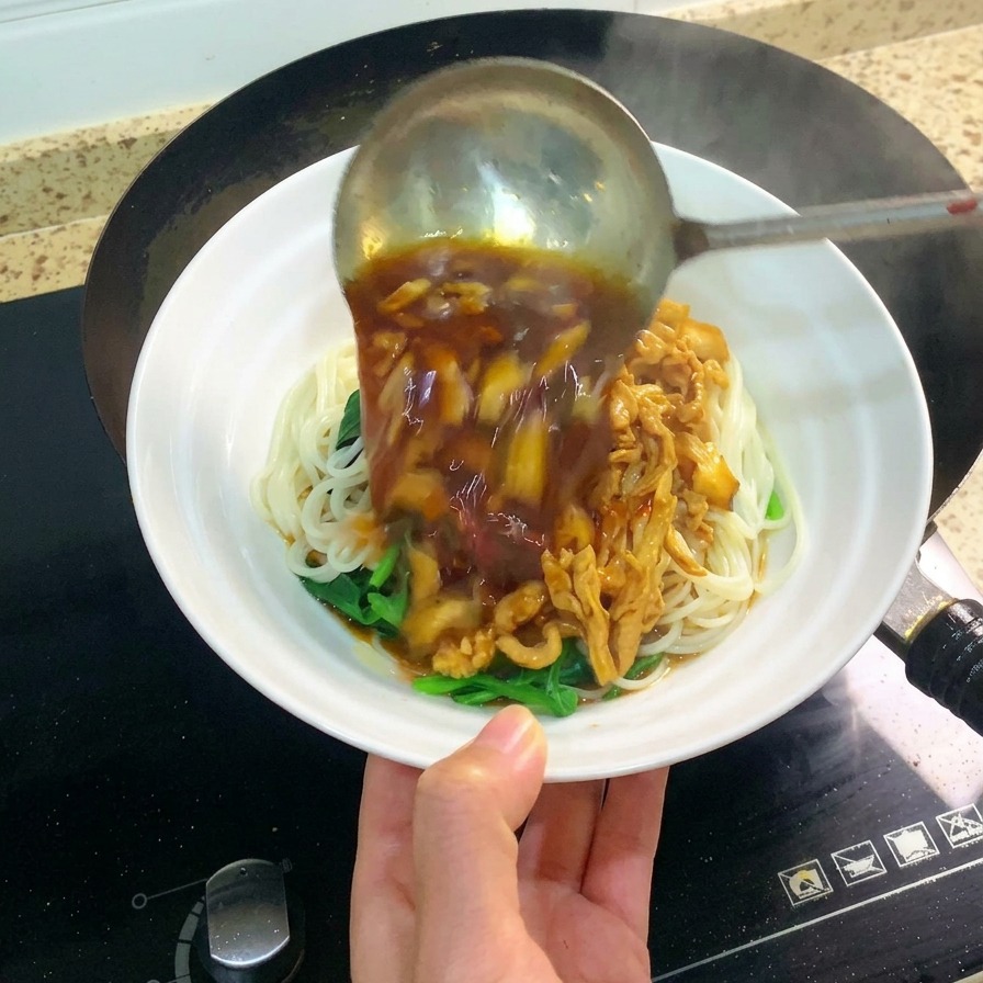 Eine große Schöpfkelle gießt die dunkle, herzhafte Hähnchen-Pilz-Sauce über Weizennudeln in einer weißen Schüssel.