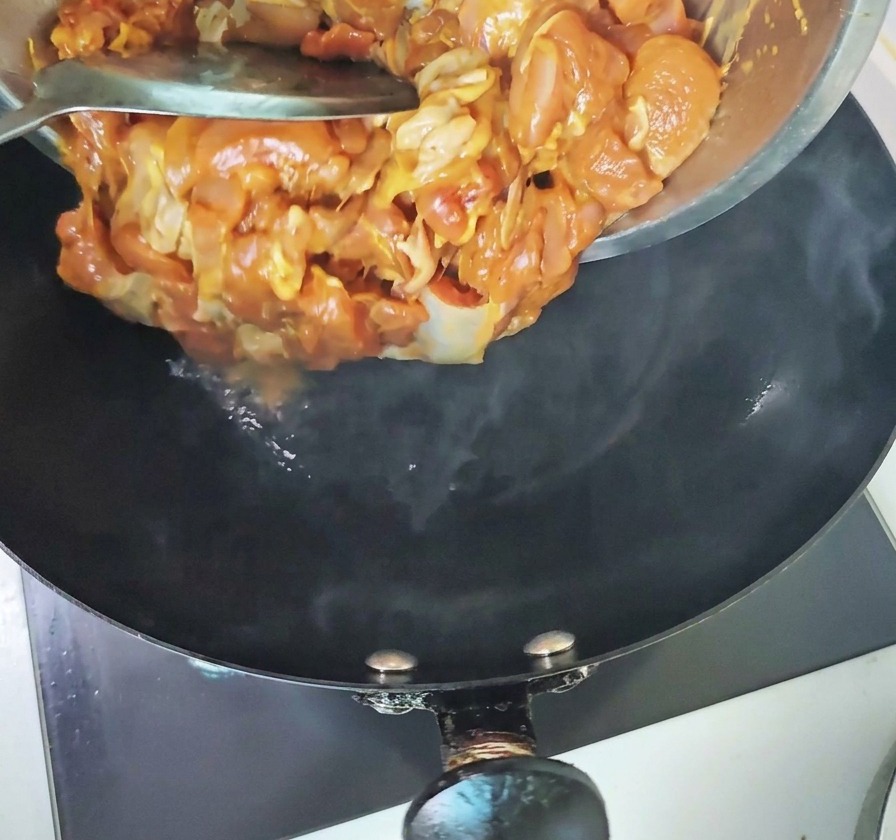 Mariniertes Hähnchenfleisch wird aus einer Metallschüssel in einen heißen, dampfenden schwarzen Wok gegeben.