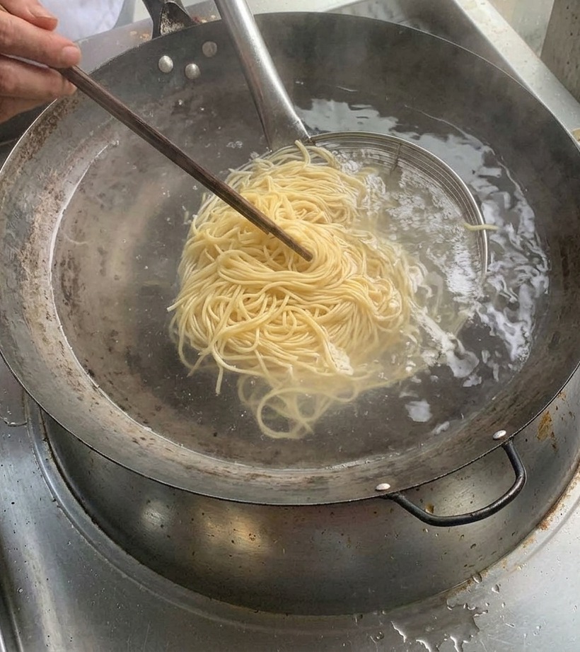 Gekochte Nudeln in einem Metallsieb über einem Topf mit kochendem Wasser.