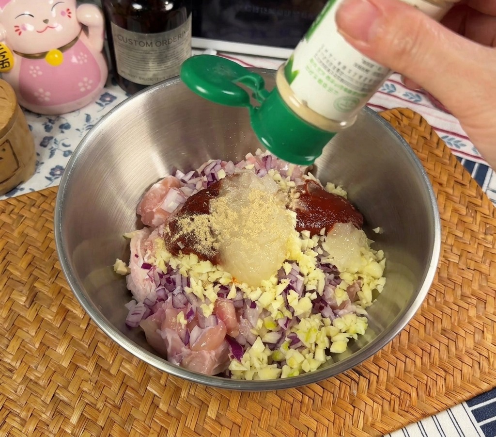 Jemand streut weißes Pfefferpulver in eine Schüssel mit rohem Hähnchen und roten Zwiebeln.