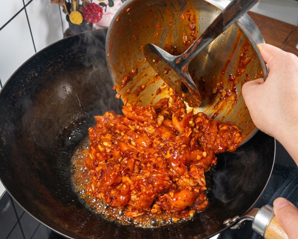 Das marinierte Hähnchenfleisch wird in einen heißen, dampfenden Wok gegeben.