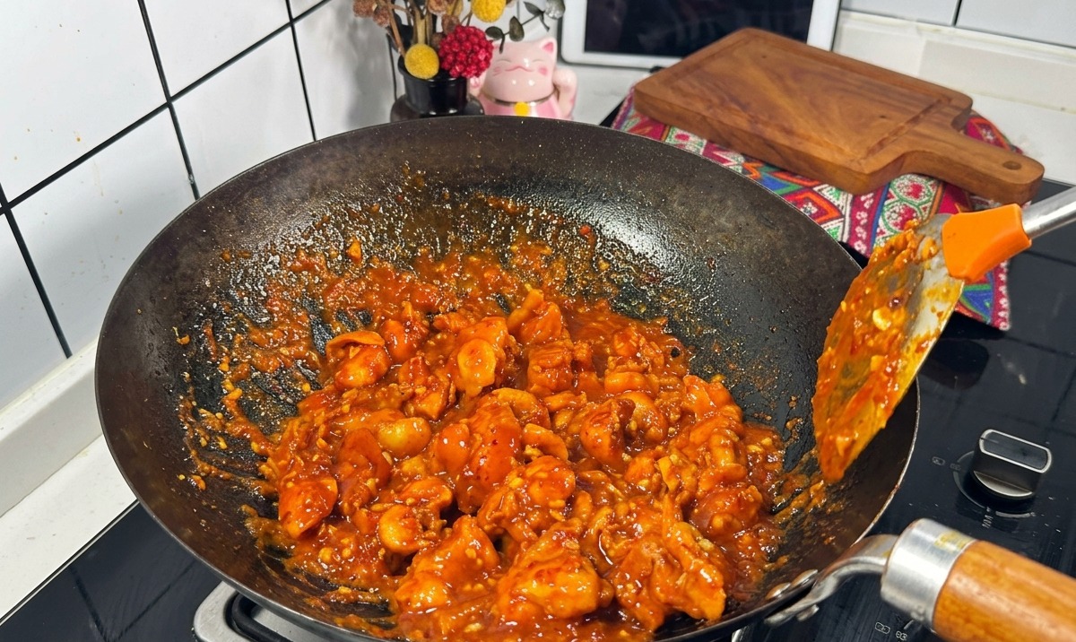 Hähnchenstücke in einer dicken, blubbernden roten Sauce werden in einem Wok gebraten.