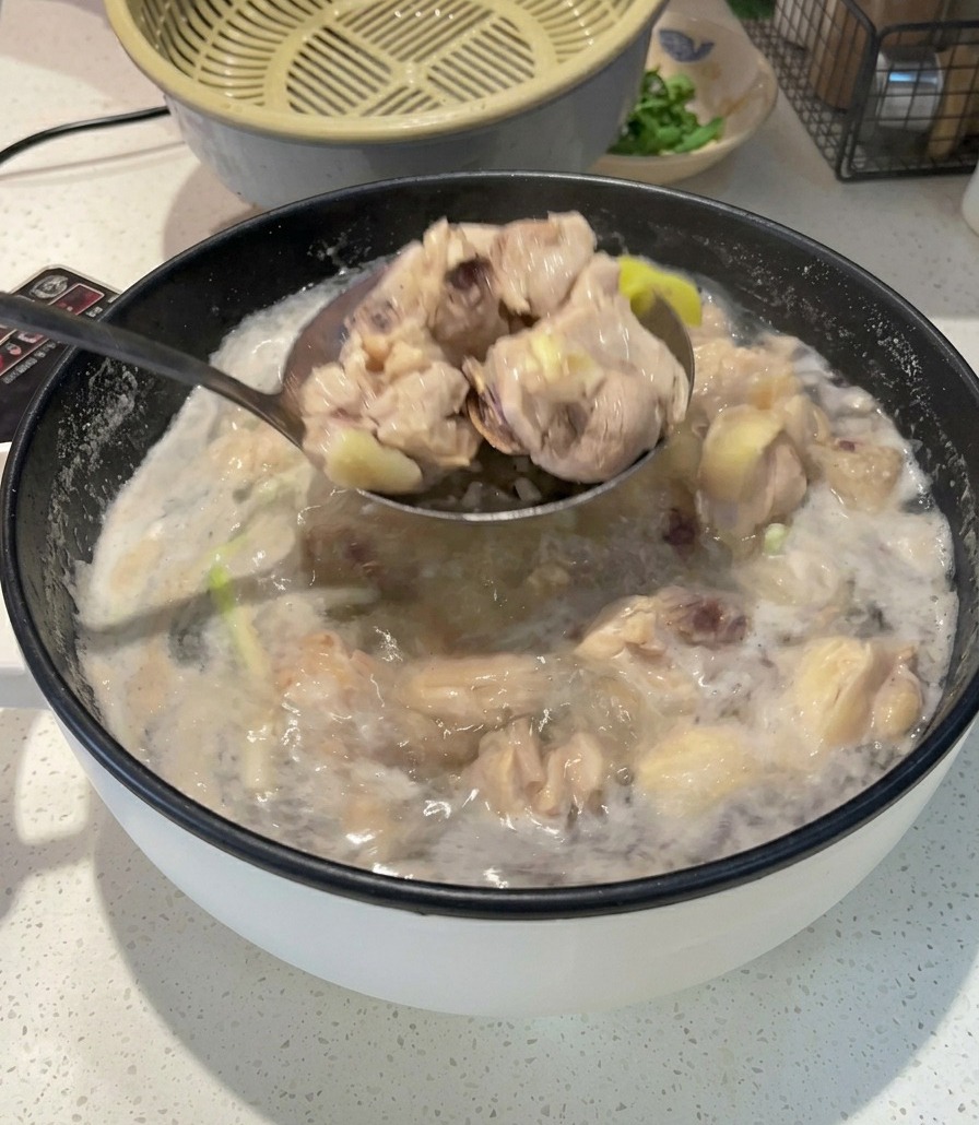 Eine Metallkelle hebt blanchierte, weiße Hähnchenstücke aus einem Topf mit kochendem, schaumigem Wasser.
