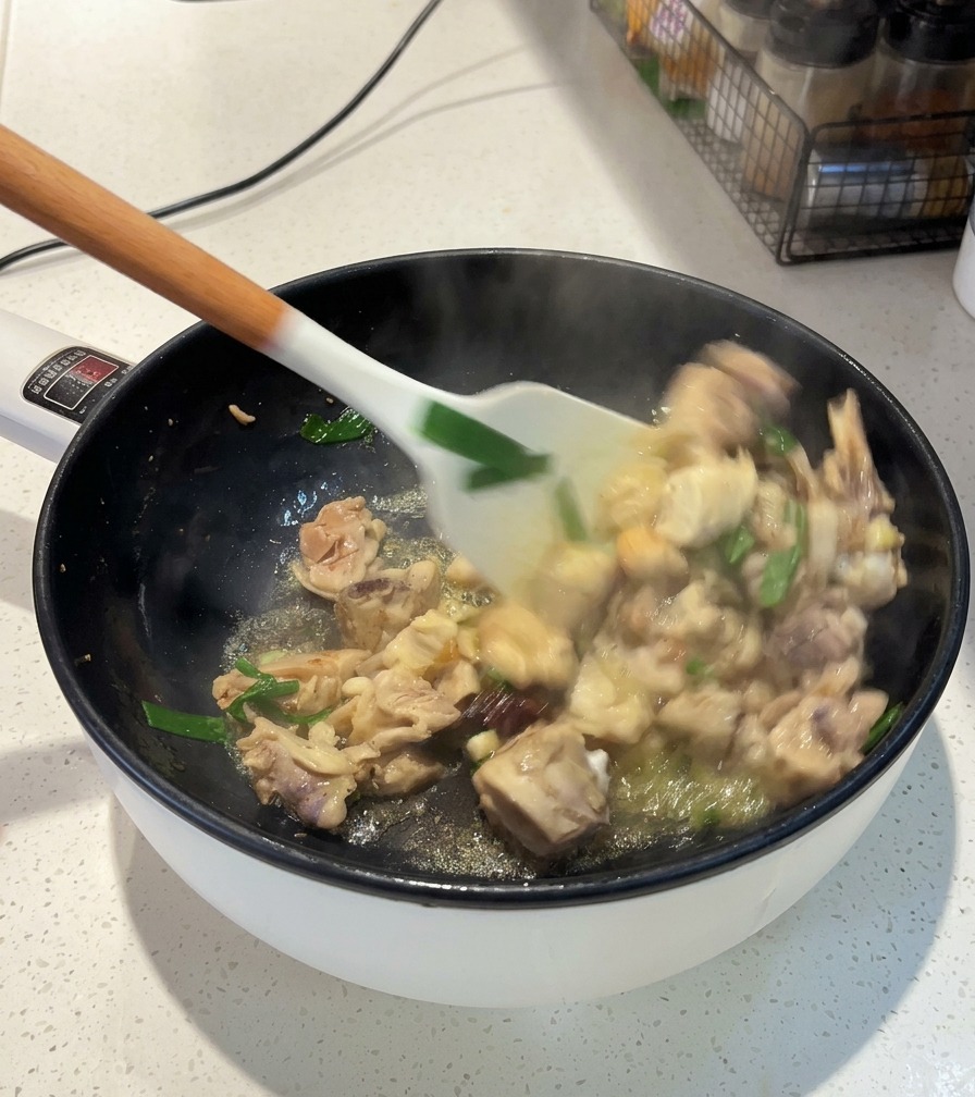 Ein weißer Pfannenwender rührt Hähnchenstücke, Frühlingszwiebeln und Sternanis in einer Pfanne über der Hitze.