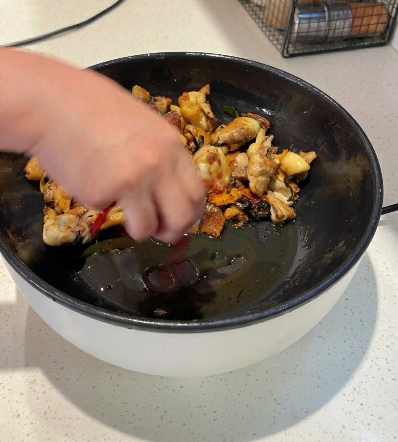 Jemand brät Hähnchenstücke in einer schwarzen Pfanne mit ganzen getrockneten roten Chilis und leuchtend rotem Chilipulver an.