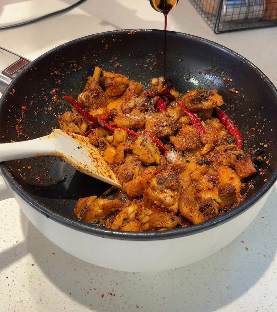 Dunkle Sojasauce wird aus einer Flasche in eine Pfanne mit scharfen Hähnchenstücken gegossen.