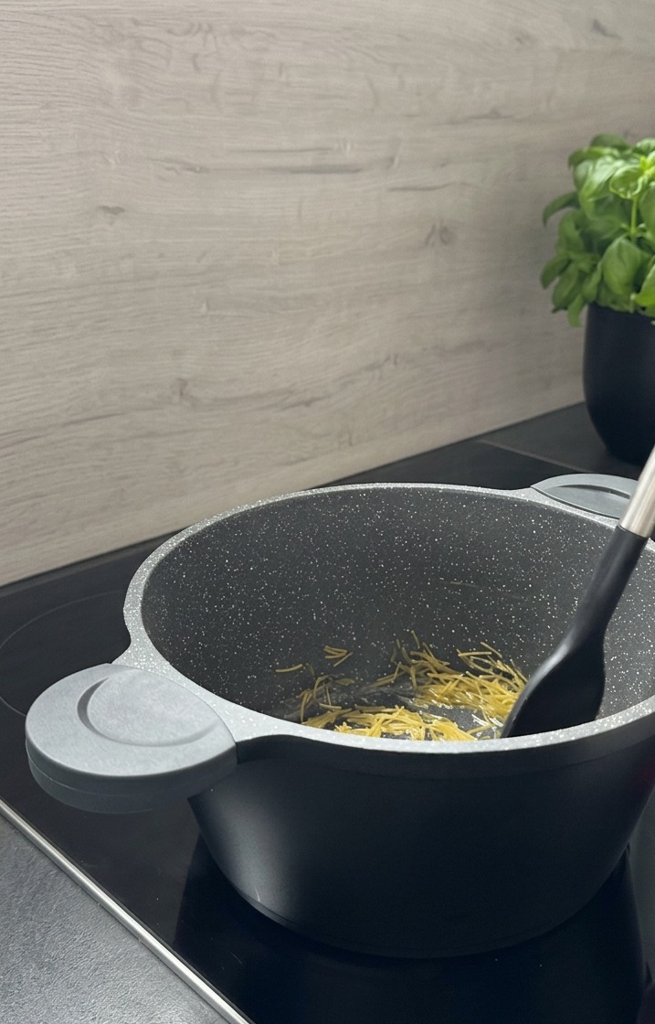 Kleine risoniförmige Nudeln werden mit einem schwarzen Pfannenwender in einem grauen Topf mit Granitmuster goldbraun angebraten.