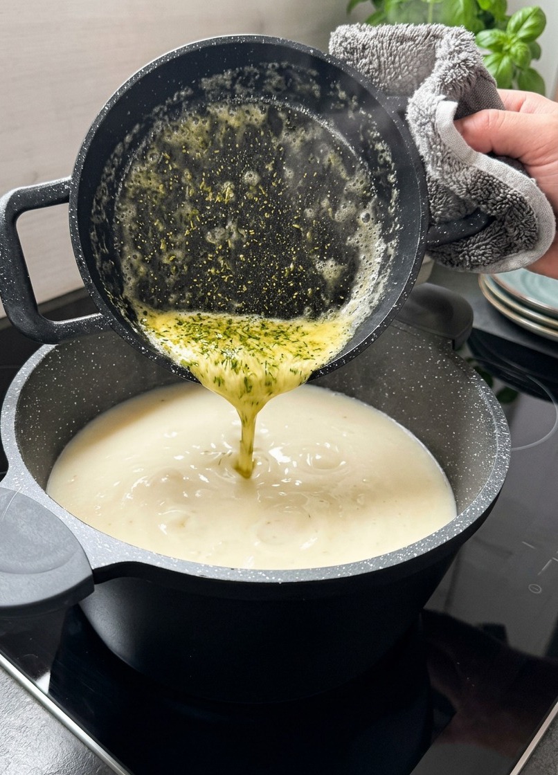 Geschmolzene gelbe Butter mit grünen getrockneten Minzflocken wird aus einem kleinen schwarzen Topf in eine cremige weiße Suppe gegossen.