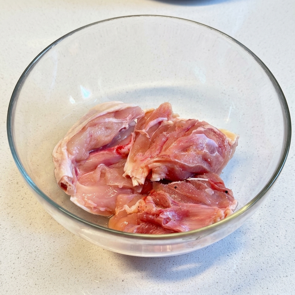 Rohe Hähnchenschenkel werden in einer transparenten Glasschüssel großzügig mit Salz und Pfeffer bestreut.