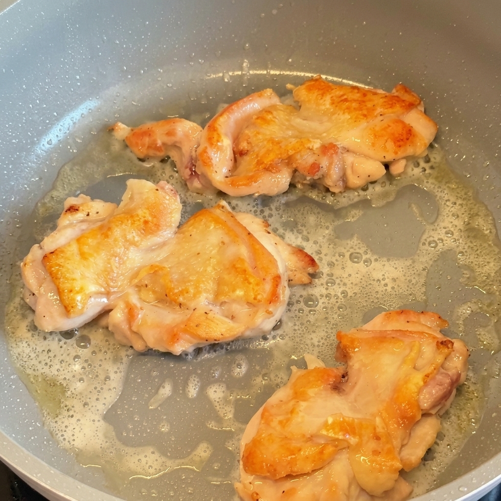 Drei Hähnchenschenkel braten in einer Pfanne und wurden gewendet, um die knusprige, goldbraune Haut zu zeigen.