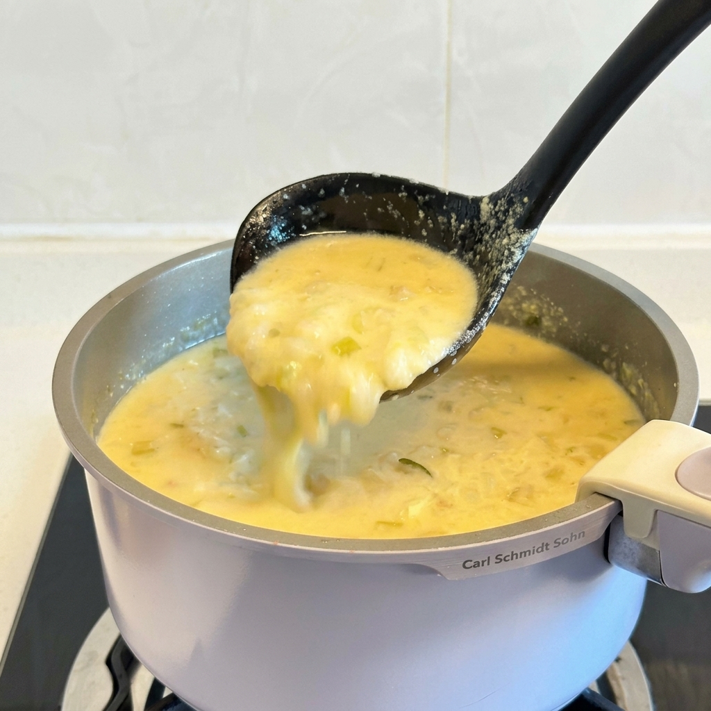 Eine schwarze Schöpfkelle hebt eine Portion der dicken, cremig-gelben griechischen Zitronen-Hühnersuppe aus dem Topf.