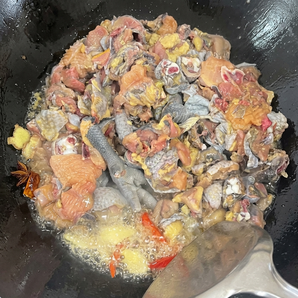 Nahaufnahme von Seidenhuhnstücken, die mit Gewürzen im Wok geschwenkt werden; brutzelndes Öl und der Würzprozess sind sichtbar.