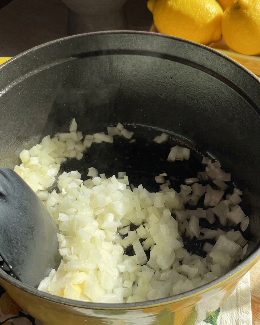 Gewürfelte weiße Zwiebeln werden in einem dunklen Kochtopf umgerührt, während sie in Butter weich dünsten.